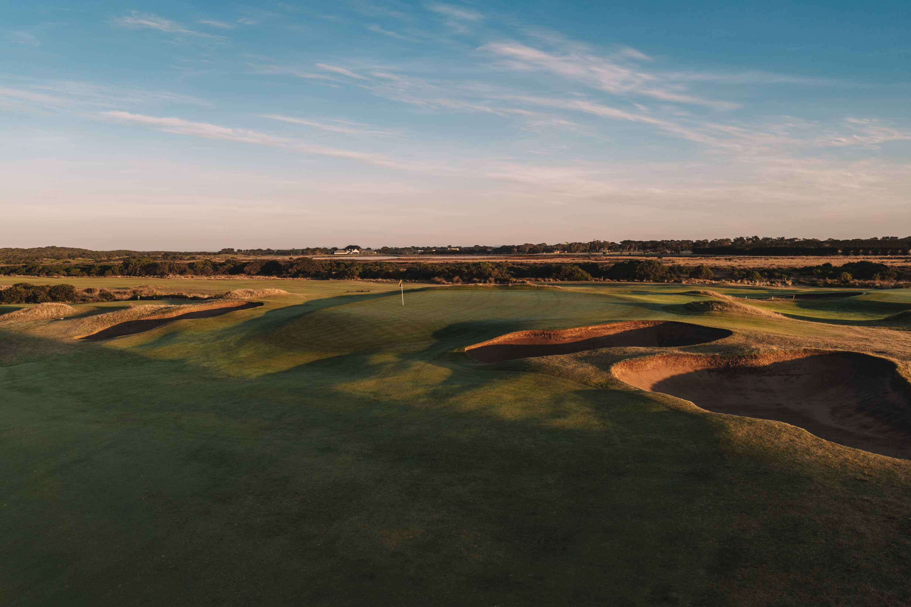 Bunkers and a green under a blue sky, late in the day